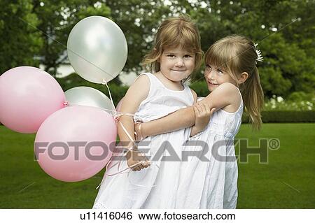 Stock Photograph - Two young girls in garden, one raising other, portrait. Fotosearch