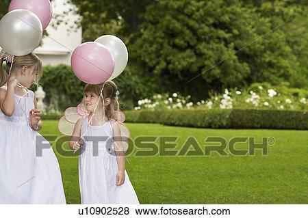 Two young girls in garden, wearing white dresses, holding balloons View Large Photo Image Stock Photo - Two young girls in garden, wearing white dresses, holding balloons. Fotosearch