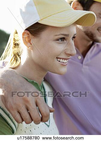 Stock Image - Two young golfers on court, focus on smiling woman. Fotosearch