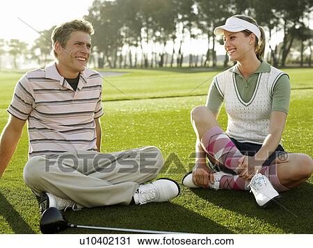 Stock Image - Two young golfers sitting on court, smiling. Fotosearch