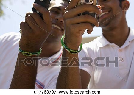 Two young men with wristbands holding mobile phones View Large Photo Image Stock Photo - Two young men with wristbands holding mobile phones. Fotosearch