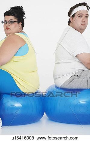 Stock Photo - Unhappy overweight man and woman sitting back to back on exercise balls, portrait. Fotosearch