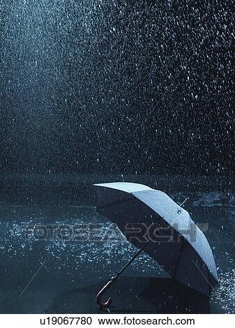 Stock Image - Unused umbrella, lying on ground being rained upon. Fotosearch