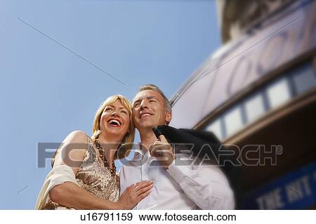 Stock Photo - Well dressed smiling couple standing by building outdoors, low angle view. Fotosearch