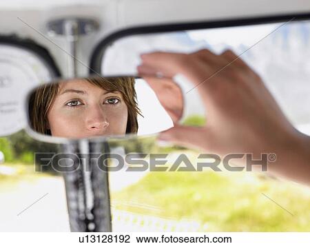 Stock Image - Woman Adjusting Rear view Mirror, close up of hand, focus on reflection in mirror. Fotosearch