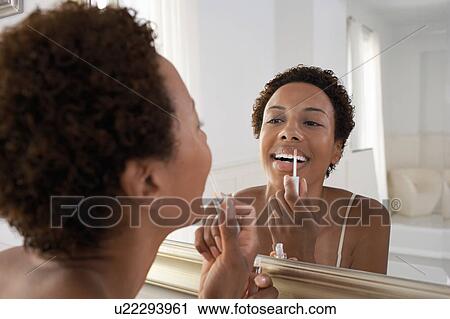 Woman applying lip gloss in mirror, at home View Large Photo Image Stock Image - Woman applying lip gloss in mirror, at home. Fotosearch