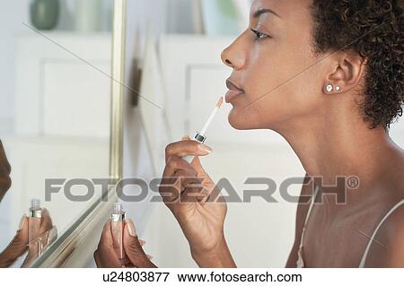 Stock Photo - Woman applying lip gloss in mirror, close-up. Fotosearch
