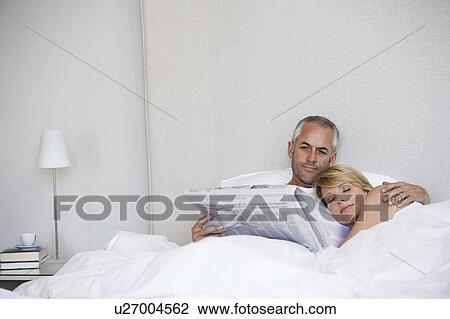 Woman embracing man reading paper in bed View Large Photo Image Stock Image - Woman embracing man reading paper in bed. Fotosearch