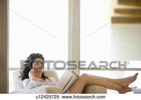 Woman holding book, sitting on armchair by window, indoors View Large Photo Image Stock Photography - Woman holding book, sitting on armchair by window, indoors. Fotosearch