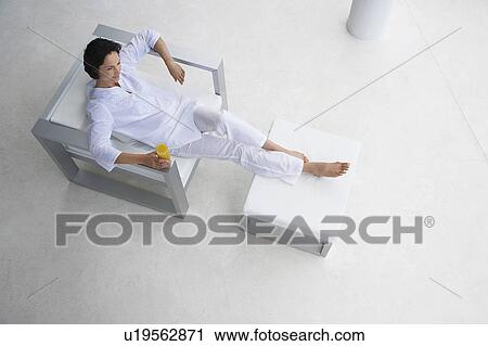 Woman holding glass of juice, reclining in armchair, elevated view View Large Photo Image Stock Image - Woman holding glass of juice, reclining in armchair, elevated view. Fotosearch