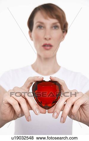 Stock Photo - Woman holding heart-shaped jewel between fingers and thumbs. Fotosearch