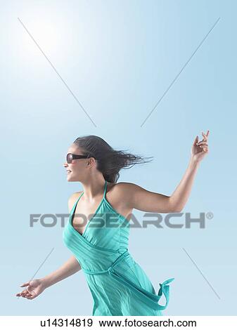 Stock Photo - Woman in dress, arms outstretched, enjoying Sunshine, side view. Fotosearch