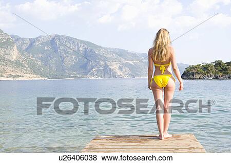 Woman in yellow bikini stands at edge of lake View Large Photo Image Stock Photo - Woman in yellow bikini stands at edge of lake. Fotosearch