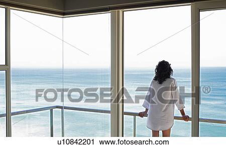 Stock Image - Woman looking at view, standing on balcony, back view. Fotosearch