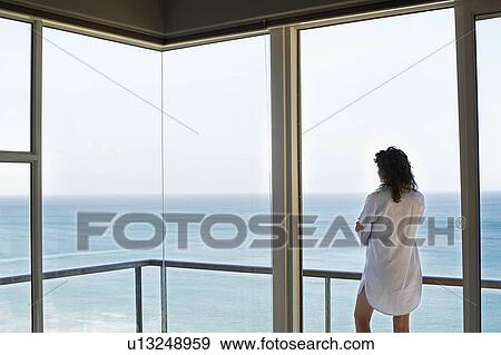 Stock Photo - Woman looking at view, standing on balcony, back view. Fotosearch