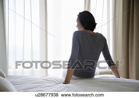 Woman looking through window, sitting on bed, back view View Large Photo Image Stock Photo - Woman looking through window, sitting on bed, back view. Fotosearch