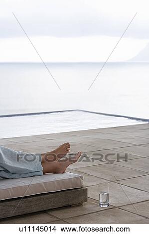 Picture - Woman lying on sun bed by infinity pool, low section. Fotosearch