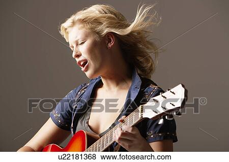Stock Photo - Woman Playing Guitar and Singing with windblown hair, close-up. Fotosearch