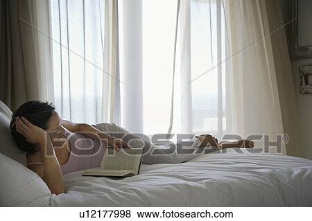 Stock Photo - Woman reading book, lying on bed. Fotosearch