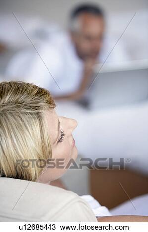 Stock Image - Woman relaxing sitting in armchair in bedroom, elevated view. Fotosearch
