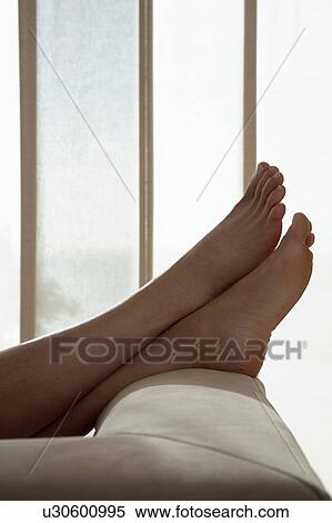 Stock Photography - Woman resting with feet up on sofa in living room, close up of feet, low section. Fotosearch
