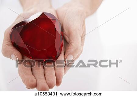Stock Image - Woman showing heart-shaped jewel, close up on hands. Fotosearch
