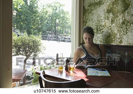 Stock Photography - Woman sits reading guidebook in Amsterdam cafe. Fotosearch
