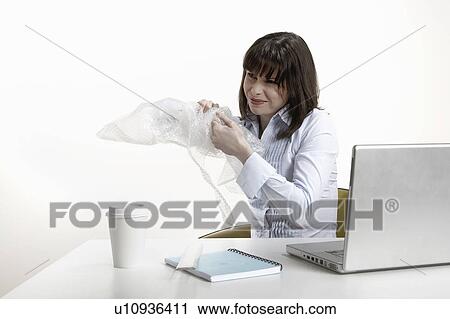 Stock Image - Woman sitting at desk, playing with bubble wrap. Fotosearch