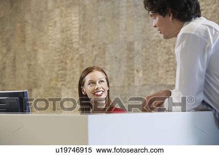 Woman sitting behind desk smiling up at man View Large Photo Image Stock Photography - Woman sitting behind desk smiling up at man. Fotosearch