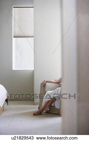 Stock Image - Woman sitting on armchair in bedroom, low section. Fotosearch