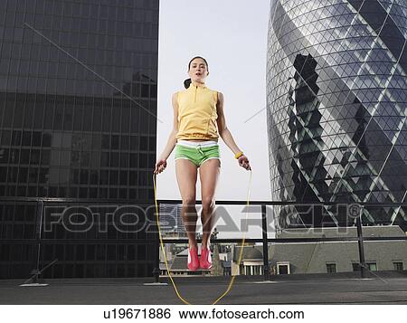 Stock Photograph - Woman skipping on skipping rope on downtown rooftop, low angle view, London, England. Fotosearch