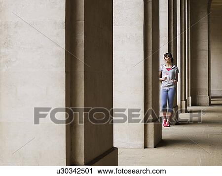 Stock Image - Woman standing against column in portico. Fotosearch