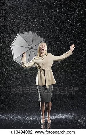 Stock Image - Woman standing in overcoat, holding umbrella, singing in the rain. Fotosearch