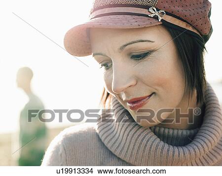 Picture - Woman standing on beach with man in background, portrait, close up. Fotosearch