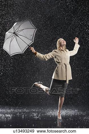 Stock Photo - Woman standing on one leg, holding umbrella, leaning into falling rain. Fotosearch