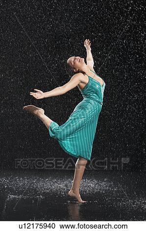 Stock Image - Woman standing on one leg, leaning into falling rain. Fotosearch