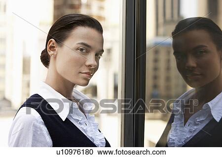 Stock Image - Woman standing outdoors, reflected in window, head and shoulders. Fotosearch