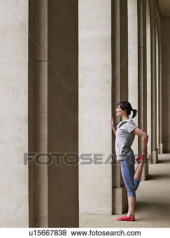 Stock Photo - Woman stretching in portico, side view. Fotosearch
