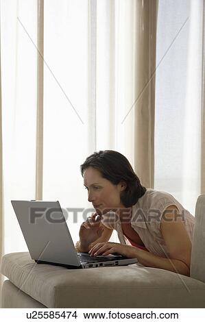 Woman using laptop, leaning on sofa cushion View Large Photo Image Picture - Woman using laptop, leaning on sofa cushion. Fotosearch
