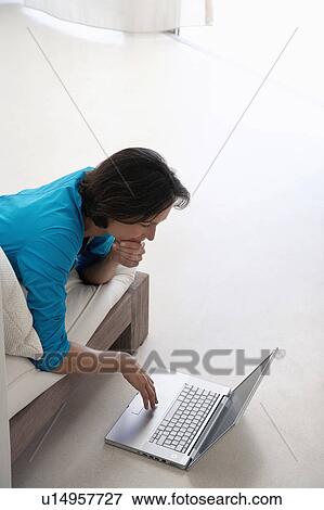 Woman using laptop, lying on sofa in living room, elevated view View Large Photo Image Stock Photo - Woman using laptop, lying on sofa in living room, elevated view. Fotosearch