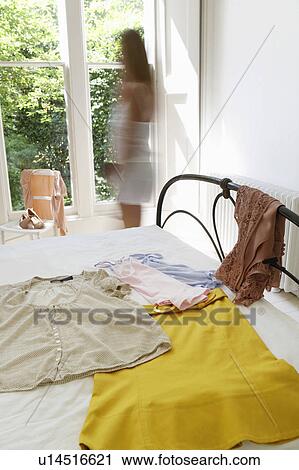 Stock Image - Woman walking by outfit laid out on bed. Fotosearch