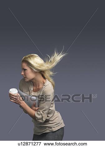 Stock Photo - Woman with hair blowing, holding coffee, facing into wind. Fotosearch