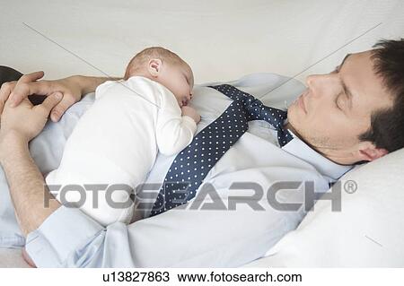 Stock Image - Working father lies sleeping with two week old. Fotosearch
