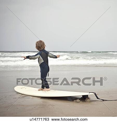 Stock Image - Young boy aged 2-3 learns how to balance on surfboard. Fotosearch