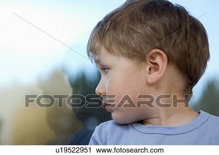 Stock Image - Young boy looking back at shadow in glass. Fotosearch