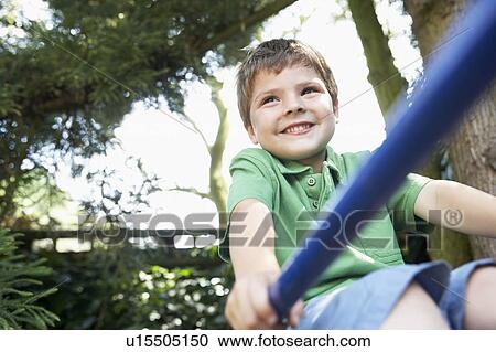 Stock Image - Young Boy sitting on monkey bars, close up. Fotosearch