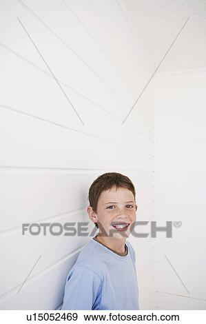 Stock Photo - Young boy standing against weather boarded wall, portrait. Fotosearch