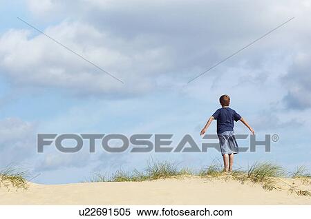 Young boy standing on sand dune in wind with arms outstretched, back view View Large Photo Image Stock Photography - Young boy standing on sand dune in wind with arms outstretched, back view. Fotosearch