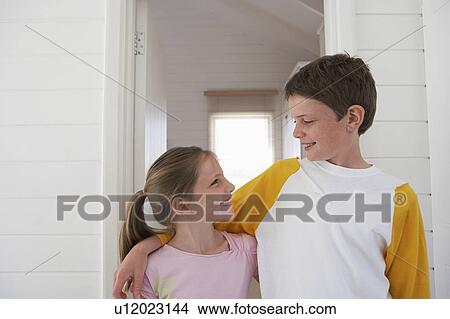 Picture - Young boy with arm around girl standing in house, half length. Fotosearch