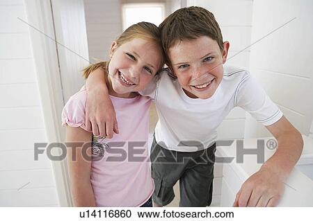 Stock Image - Young boy with arm around young girl in white room. Fotosearch